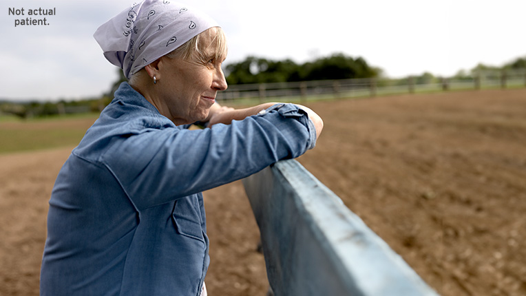 Side view of a smiling woman with a bandana leaning on a fence