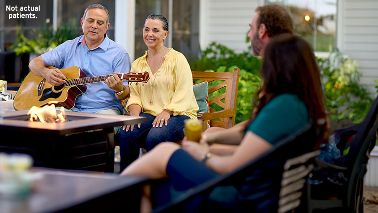 Woman sitting in a back yard around a firepit next to a man playing guitar